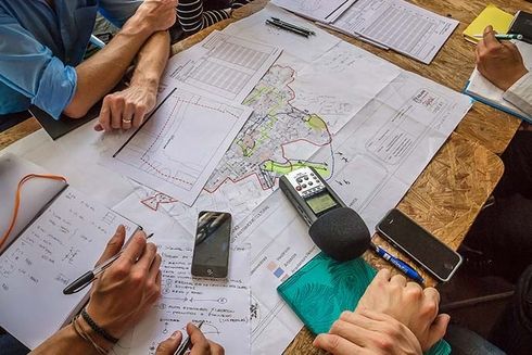 A group of people sitting around a table with papers, pens and phones