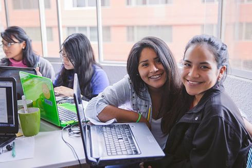 A group of teens sitting at a table with laptops and smiling