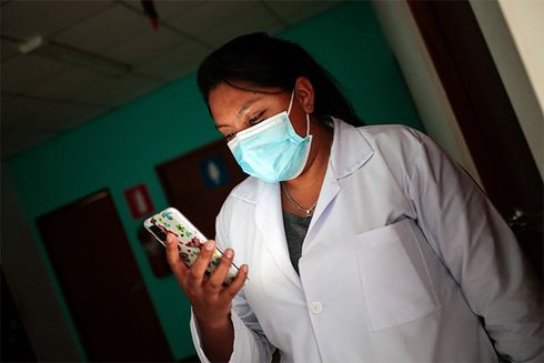 Woman wearing a mask and a white coat staring at phone