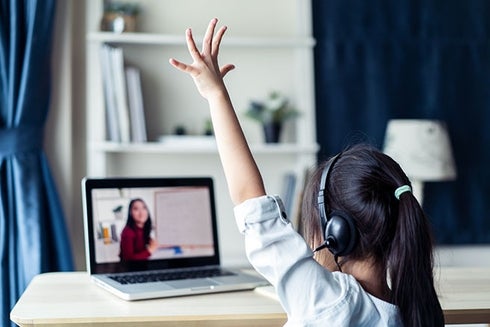 A child wearing headphones raising her hand in front of a laptop. Digital transformation - Inter-American Development Bank - IDB