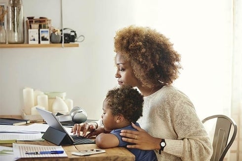 A woman holding a baby while using a laptop. Equality - Inter-American Development Bank - IDB