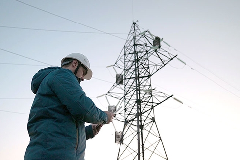 A person with safety gear standing next to a power line tower. Infrastructure - Inter-American Development Bank - IDB