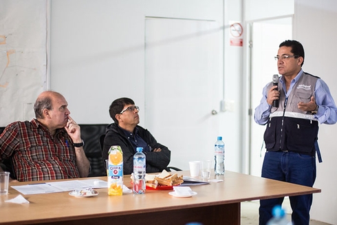 A man using a microphone with other men sitting around a table. Development - Inter-American Development Bank - IDB