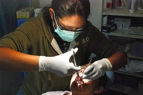 A dentist using a tool to check the teeth of a patient. Social Security - Inter-American Development Bank - IDB