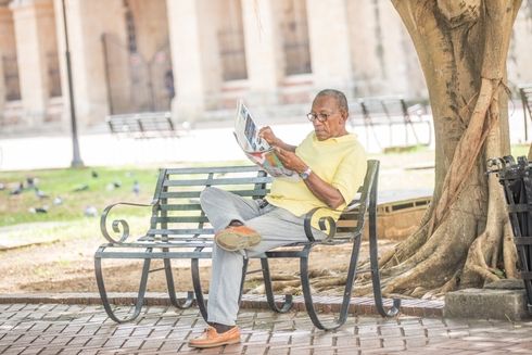 A person sitting on a bench reading a newspaper. Pension and Social Development - Inter-American Development Bank - IDB