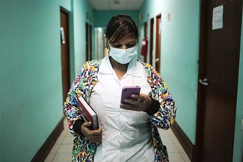 A woman wearing a mask and holding a phone. Medical Care - Inter-American Development Bank - IDB