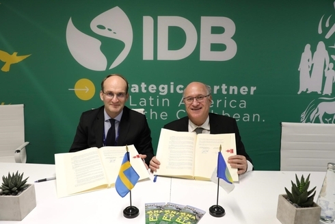 two men sitting at a table with flags and papers Climate change - Inter-American Development Bank - IDB
