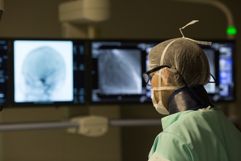 A healthcare professional in protective gear examining brain scans on monitors.