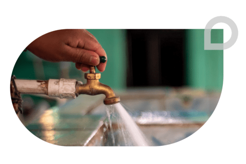 A close-up of a hand turning on a brass water tap, with clean water flowing into a sink - Inter-American Development Bank - IDB - Development Effectiveness