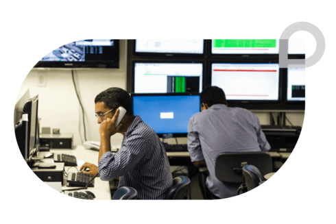 Two men working in a control room, surrounded by computer monitors displaying data and surveillance feeds - Inter-American Development Bank - IDB - Development Effectiveness