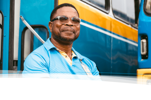 Afro-descendant man smiling warmly, with several buses visible in the background - Inter-American Development Bank IDB - Impact Development