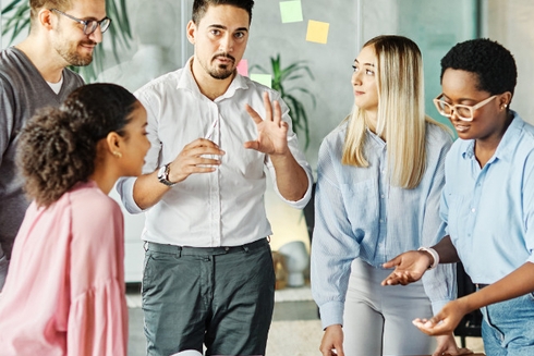 Women and men standing in front of a desk in a meeting - Inter American Development Bank - Grievances Portal