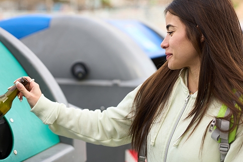 Woman throwing a glass bottle into a trash container - Inter American Development Bank - Water and Sanitation