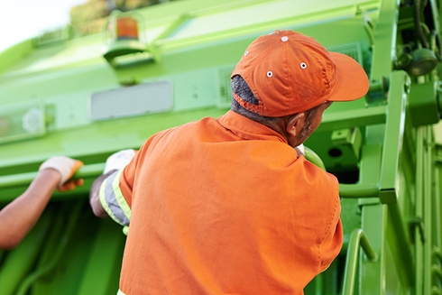 Male worker with his back turned handling a solid waste truck - Inter American Development Bank - Water and Sanitation