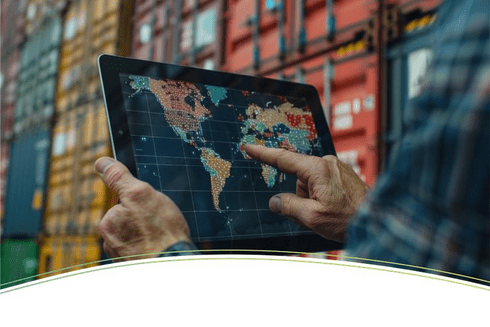 Hands holding a tablet showing a world map and merchandise in the background - Inter American Development Bank - Regional Integration