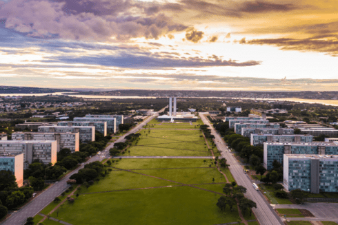 Panoramic view of green field with forest in the middle, buildings on the sides and sunset in the sky - Inter American Development Bank - Fiscal Management