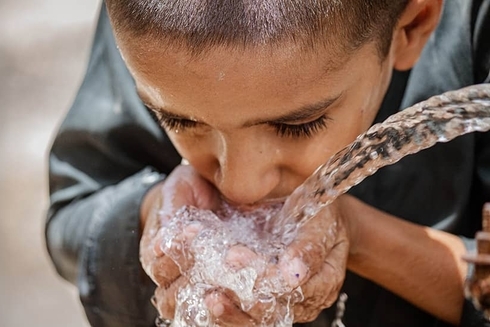 Dark-skinned boy drinking water with his hands clasped together - Inter American Development Bank - Research