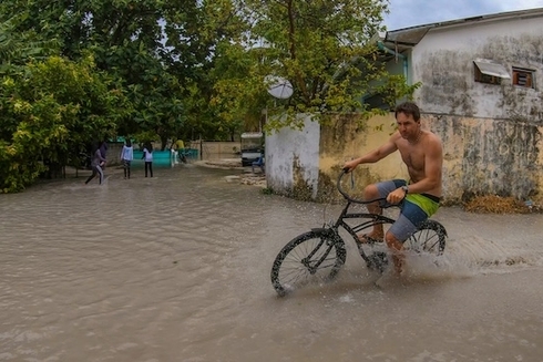 Young dark-haired man riding a bicycle through floodwaters in a working-class neighborhood - Inter American Development Bank - Social Protection