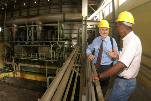 Two professionals wearing hard hats discussing operations inside an industrial facility IDB