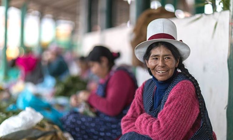 A woman smiling sitting in a market. Economic Growth - Inter-American Development Bank - IDB