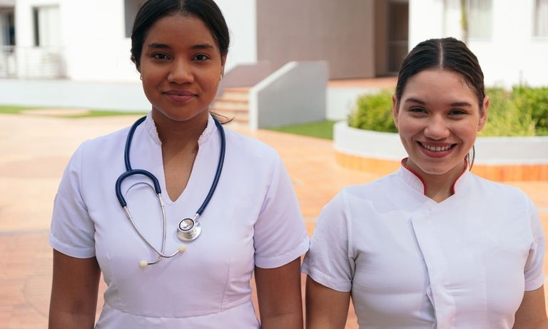 Two nurses women smiling with a hospital in the background - Inter American Development Bank - Migration