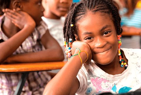 A girl smiles sitting at a desk in the classroom - Inter-American Development Bank - IDB