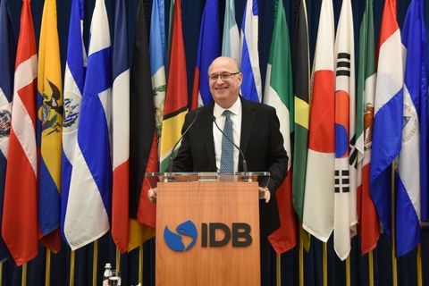 IDB President Ilan Goldfajn, shown standing in front of a podium with flags behind 